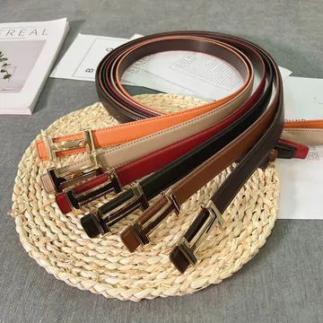 Leather belts in red, orange, white, brown and black coiled on a woven mat, with gold-tone buckles.