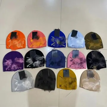 Fourteen knitted beanies in orange, blue, grey, yellow and black arranged on a white floor.